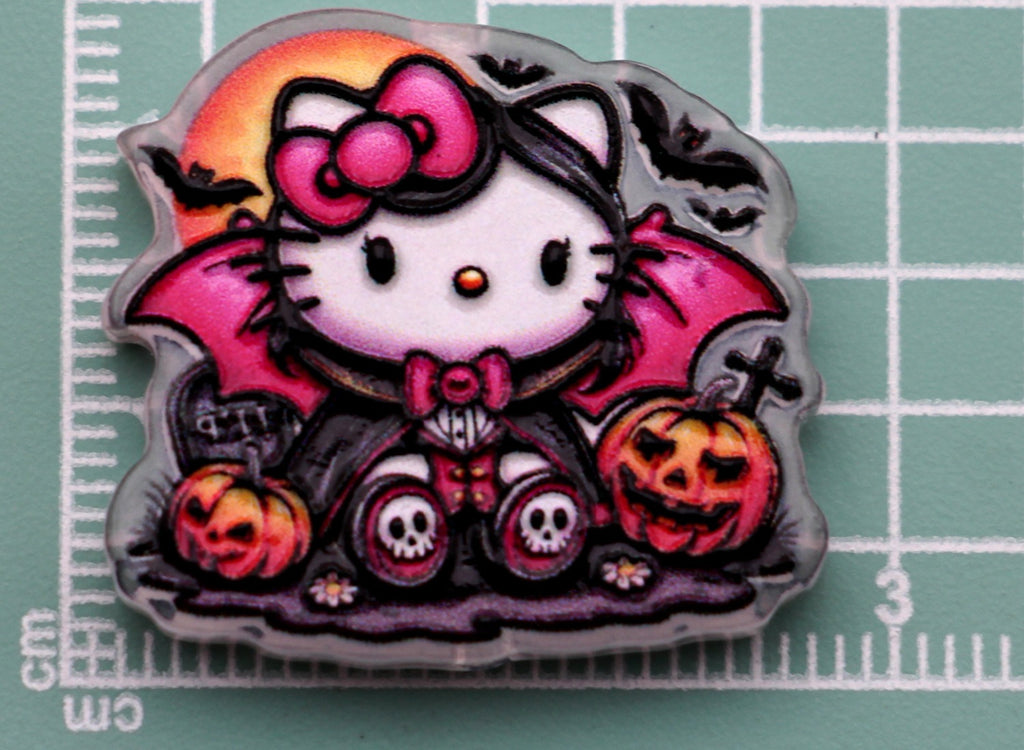Hello Kitty vampire acrylic charm with pink bow, bat wings, jack-o'-lanterns, and moon on green cutting mat