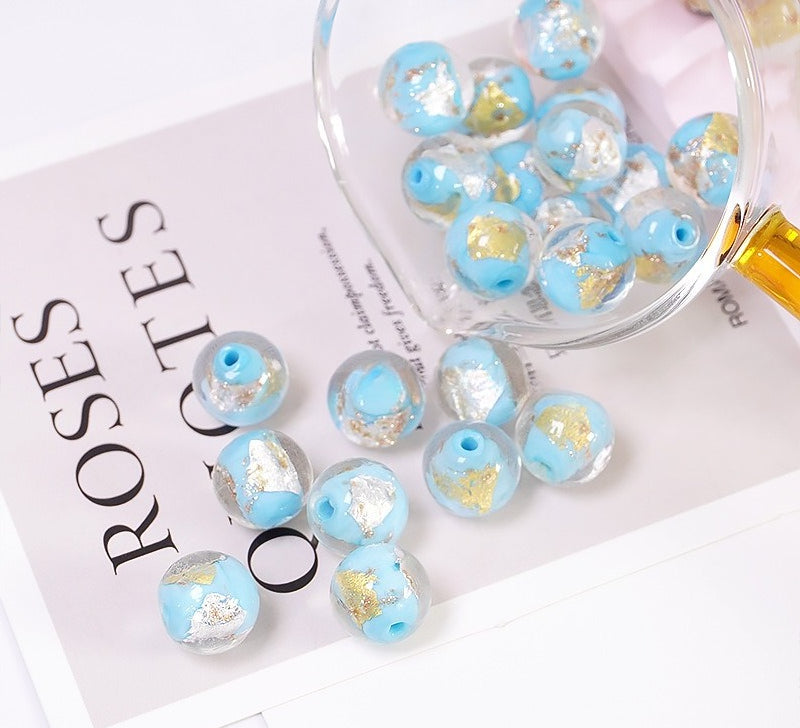 Light blue gold-foil glass beads spilling from a glass bowl onto a printed card