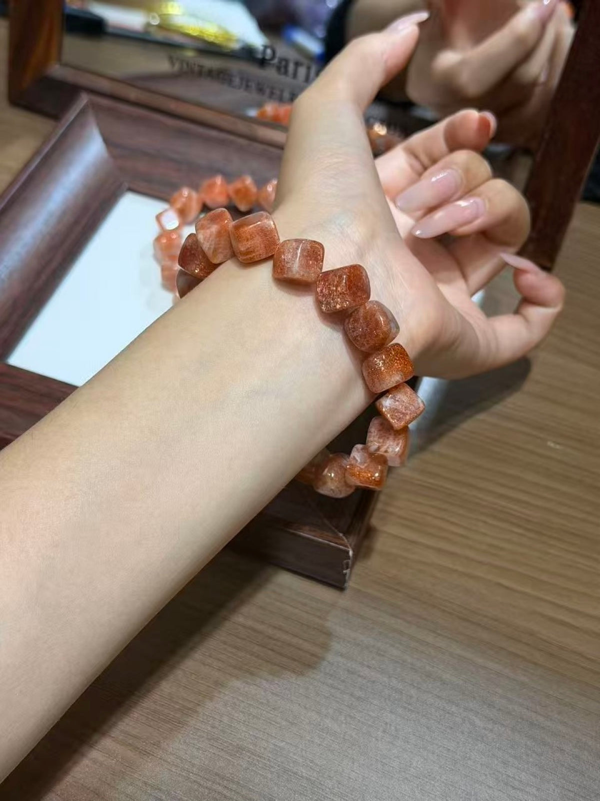 Person wearing a golden sunstone cube bracelet with sparkling peach-gold sugar cube beads on the wrist, with the matching second bracelet resting on a wooden jewelry display frame