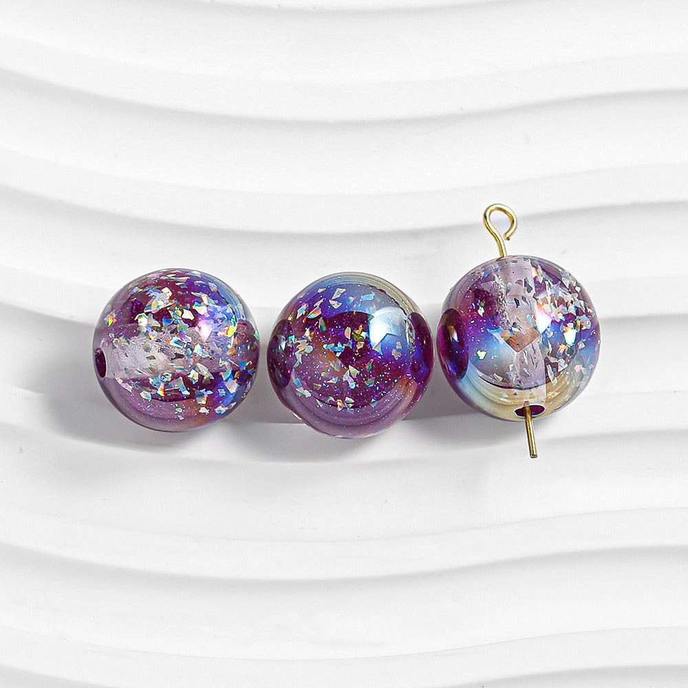 Three purple glitter resin beads on white; right bead has gold loop and pin