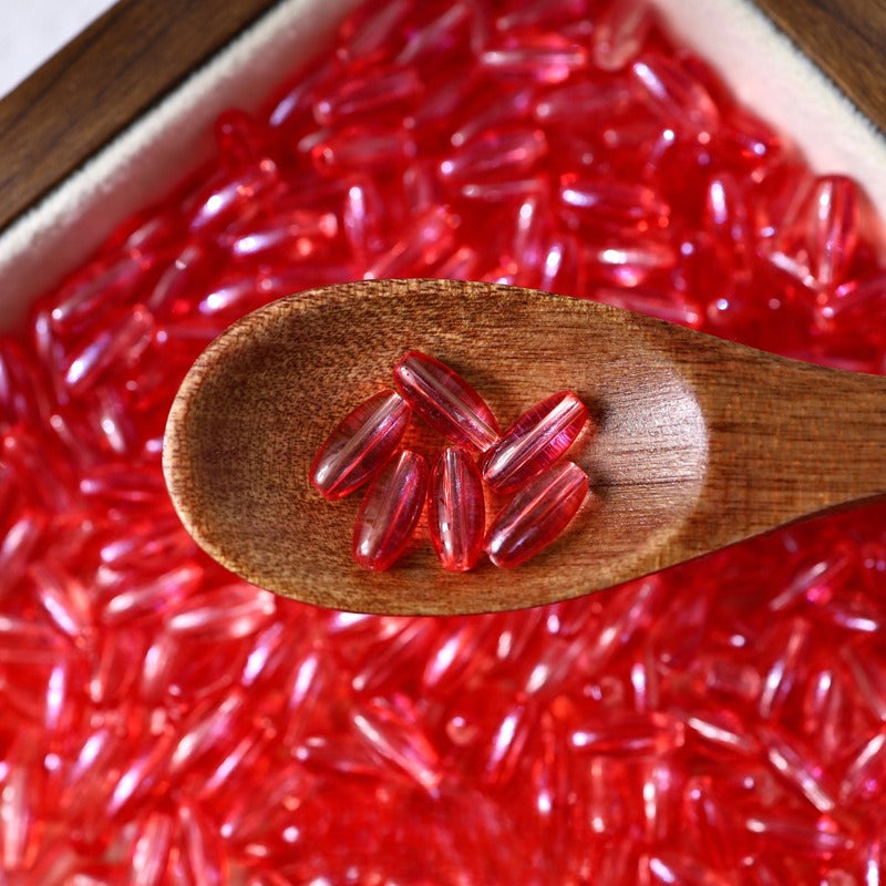 Red translucent 4x9mm glazed glass long rice beads scattered in a white dish