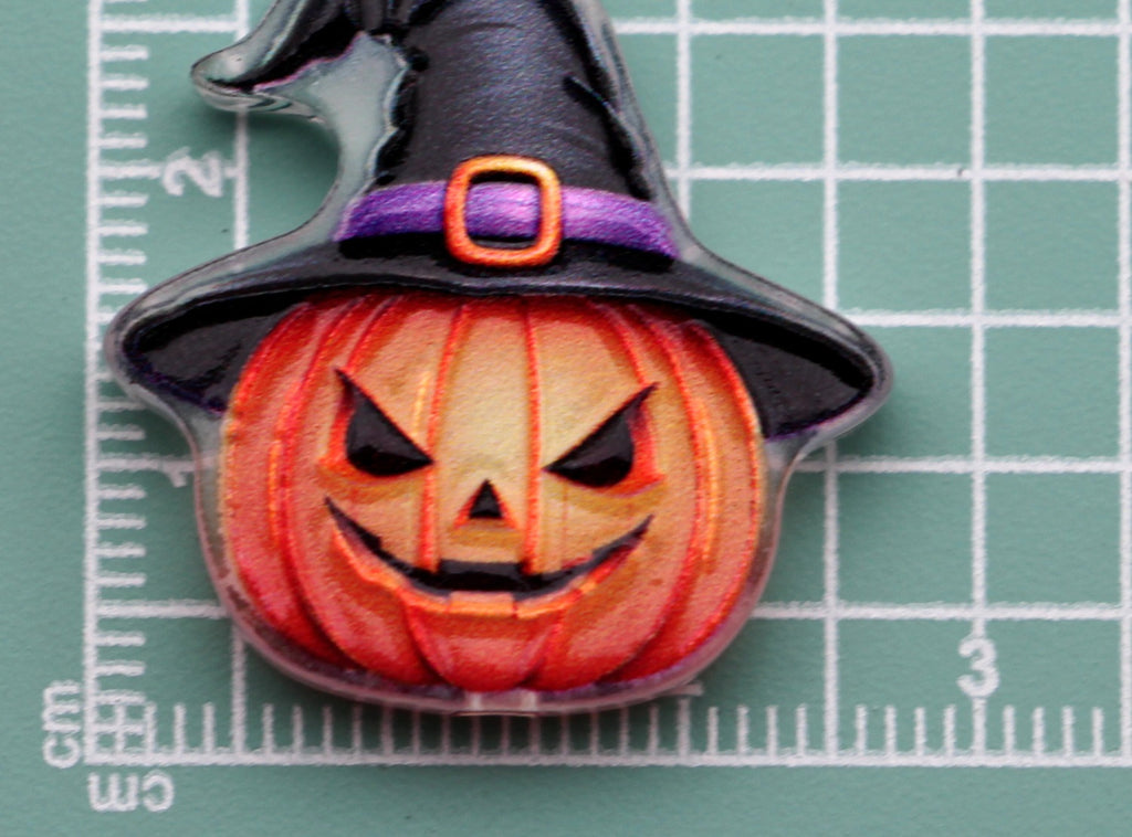 Halloween acrylic charm: carved orange pumpkin wearing a black witch hat with purple band and orange buckle, on green cutting mat