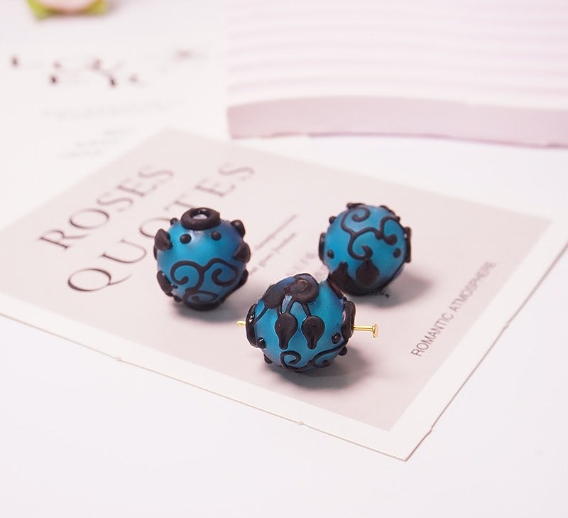 Three blue and black patterned glass bead earrings displayed on a decorative card on a white surface.