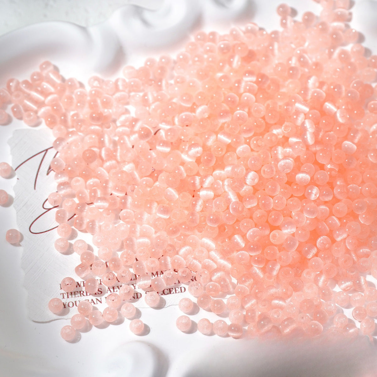 Close-up pile of frosted pink cat's-eye glass beads on white surface