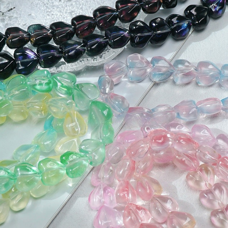 Heart-shaped glass bead strands in black, green, yellow, pink and blue on a reflective silver surface