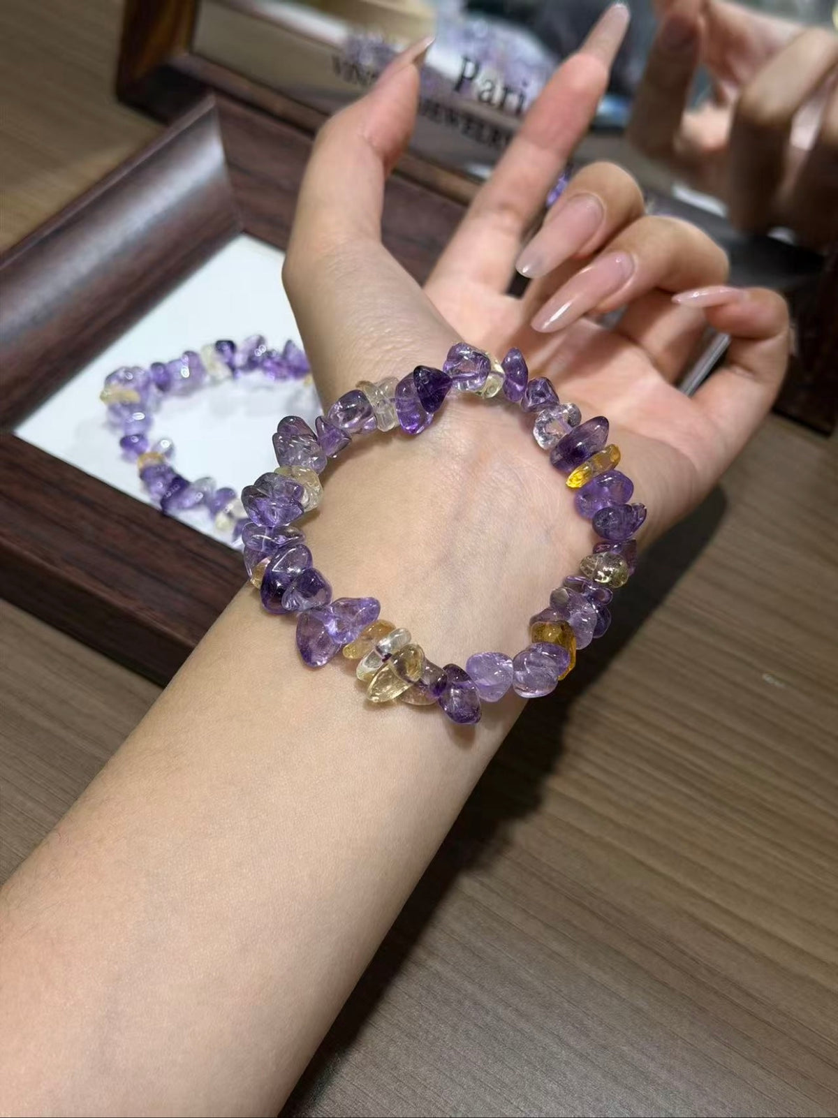 Ametrine chip bracelet worn on a wrist, with a second ametrine chip bracelet coiled in a display tray in the background