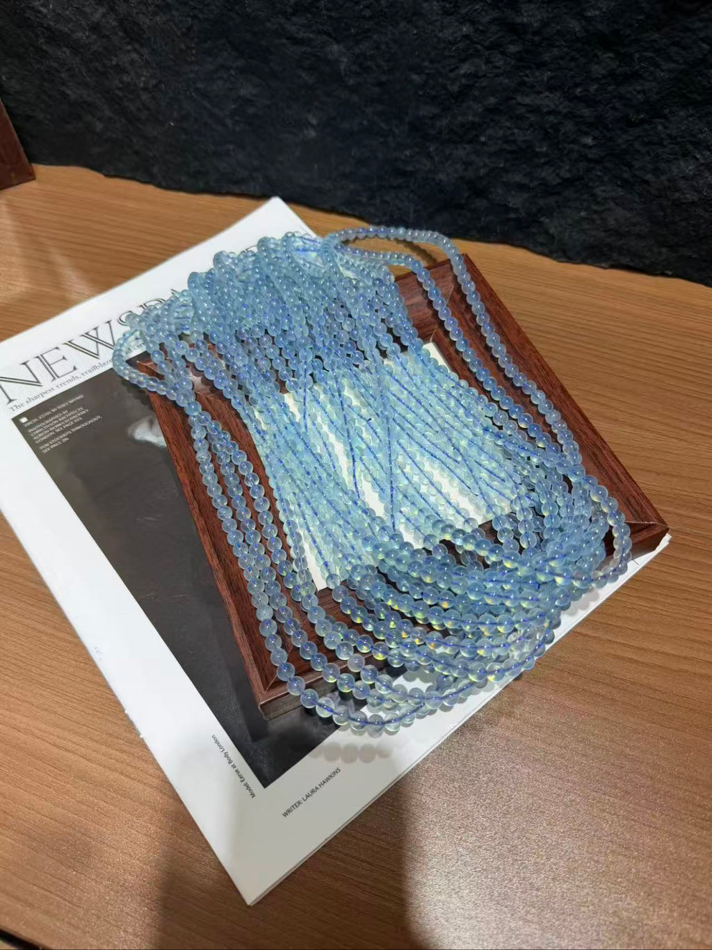 Multiple strands of pale blue aquamarine beads laid out on a wooden tray over newspaper