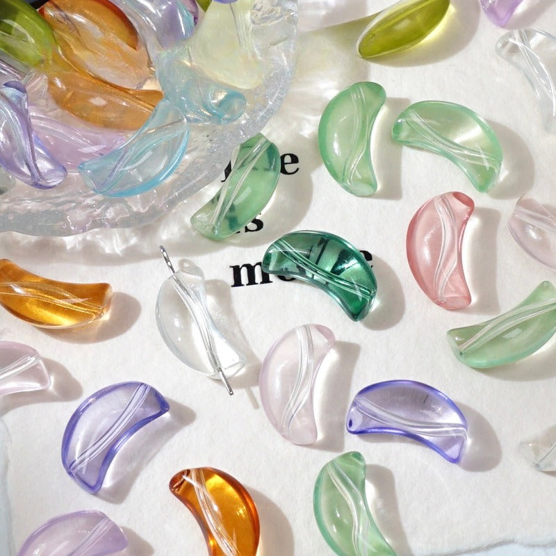 Colorful translucent crescent-shaped glass beads on white with a glass dish of more beads