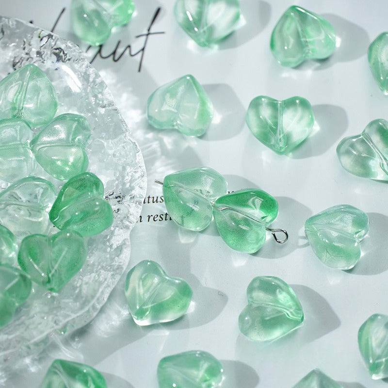 Translucent mint green heart-shaped glass beads with jump rings on a white surface