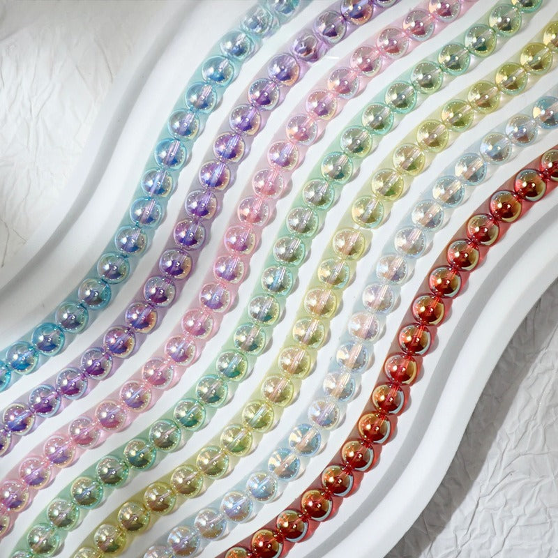 Multiple strands of iridescent round beads arranged diagonally on a white surface, showing a rainbow of colors including blue, purple, pink, green, yellow, and red.