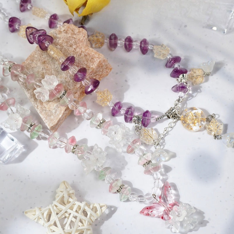 Beaded necklace with purple, pink and clear gravel beads, floral charms and butterfly pendants on a white surface