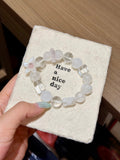 White and clear beaded bracelet with mother-of-pearl flower charm on a 'Have a nice day' card held in hand