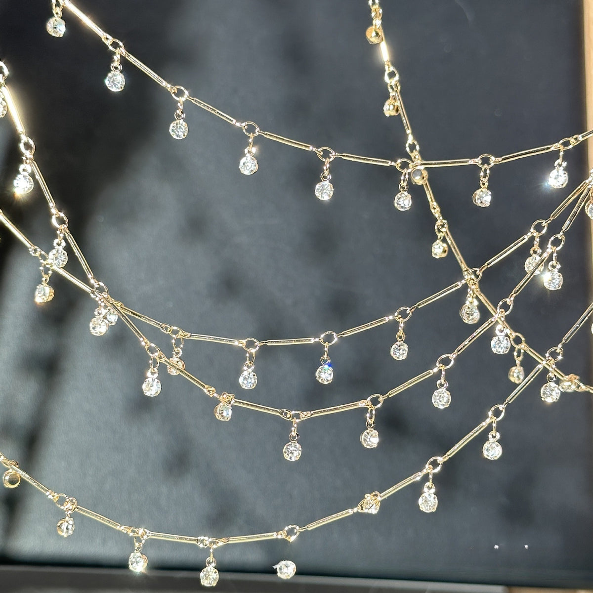 A gold-toned multi-strand chain necklace with multiple dangling clear faceted gemstones, displayed against a dark gray background.