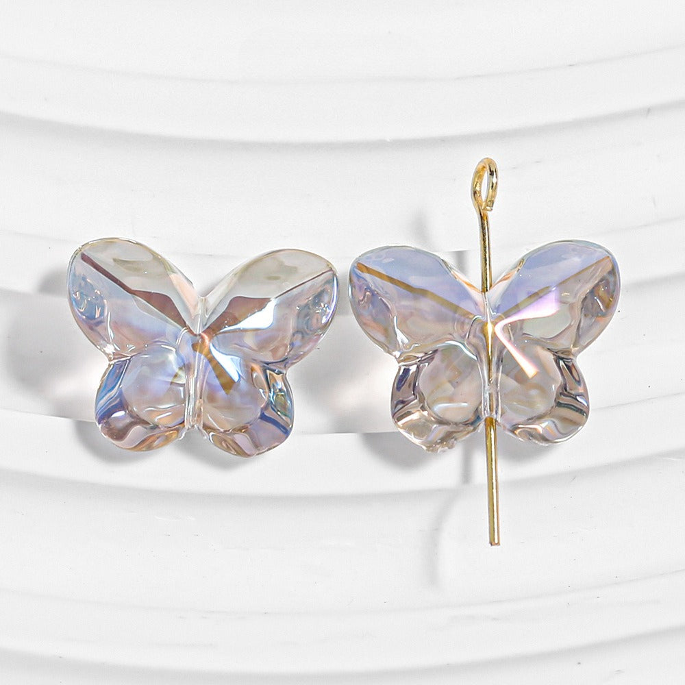 Two iridescent clear butterfly-shaped beads, one threaded on a gold headpin, on a white wavy background