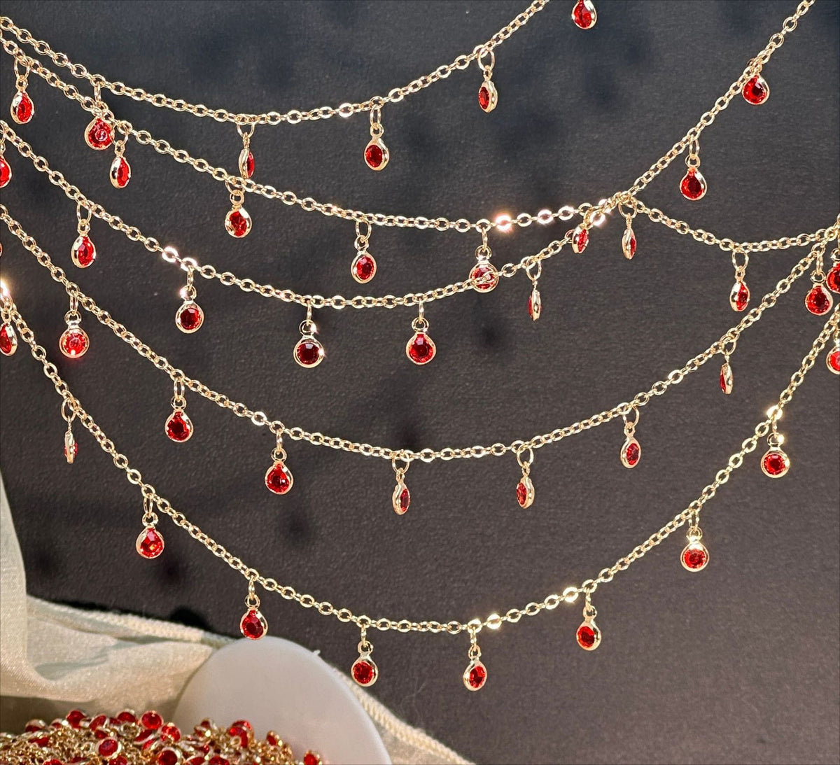 Gold chain garland with multiple draped rows of small teardrop-shaped red gemstone charms, displayed against a dark background.