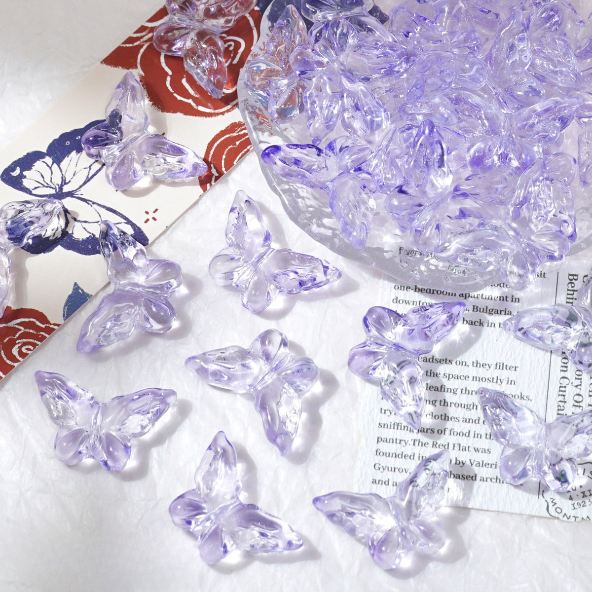 Clear butterfly-shaped glass beads scattered on white fabric surface with glass bowl