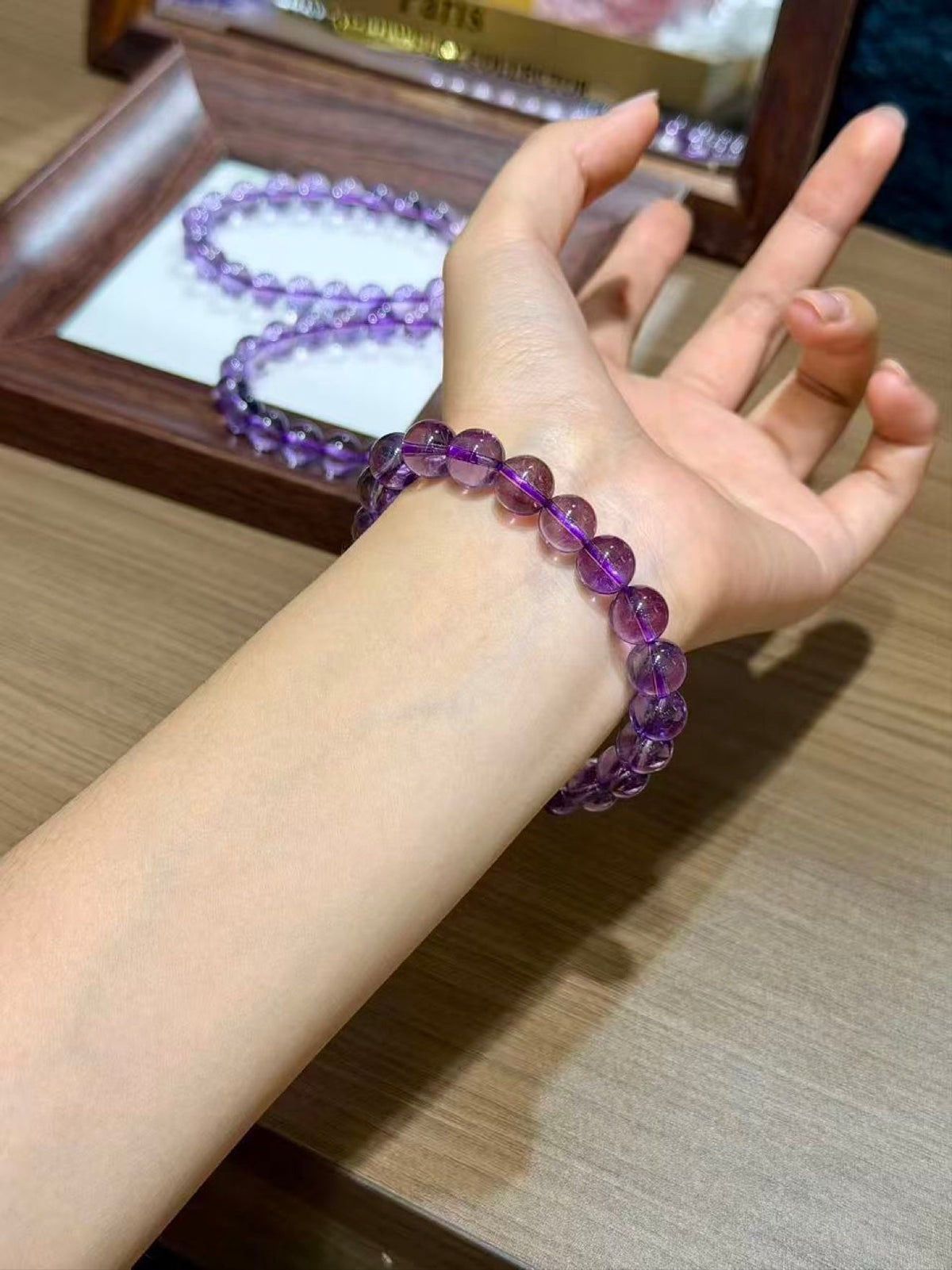 Wrist wearing purple amethyst beaded bracelet, matching bracelet in wooden jewelry box behind