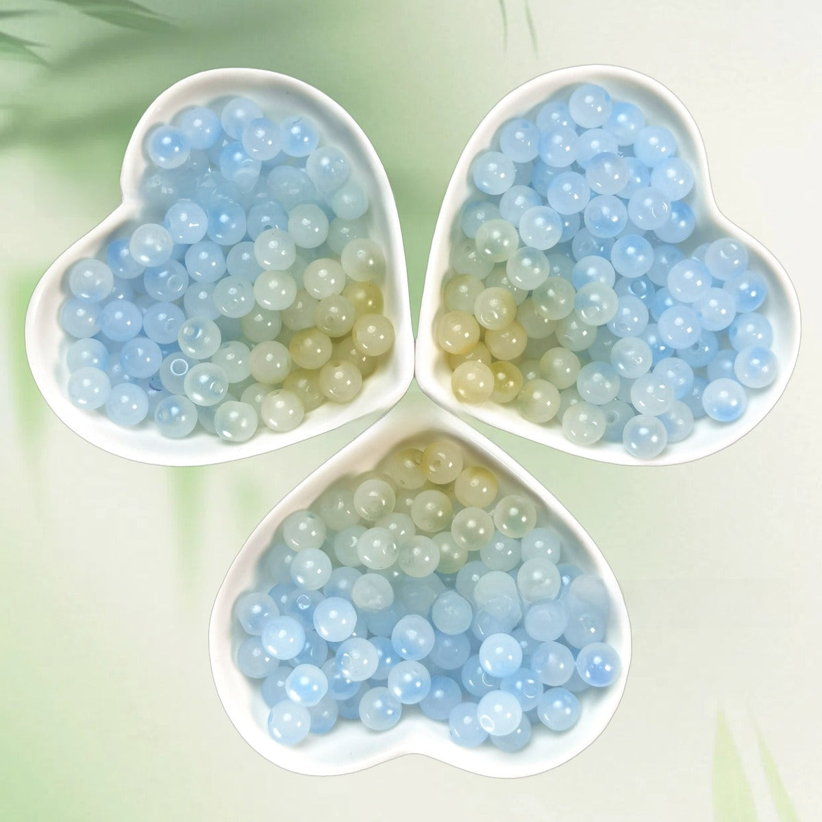 Three heart-shaped bowls of translucent blue, aqua, and pale yellow beads