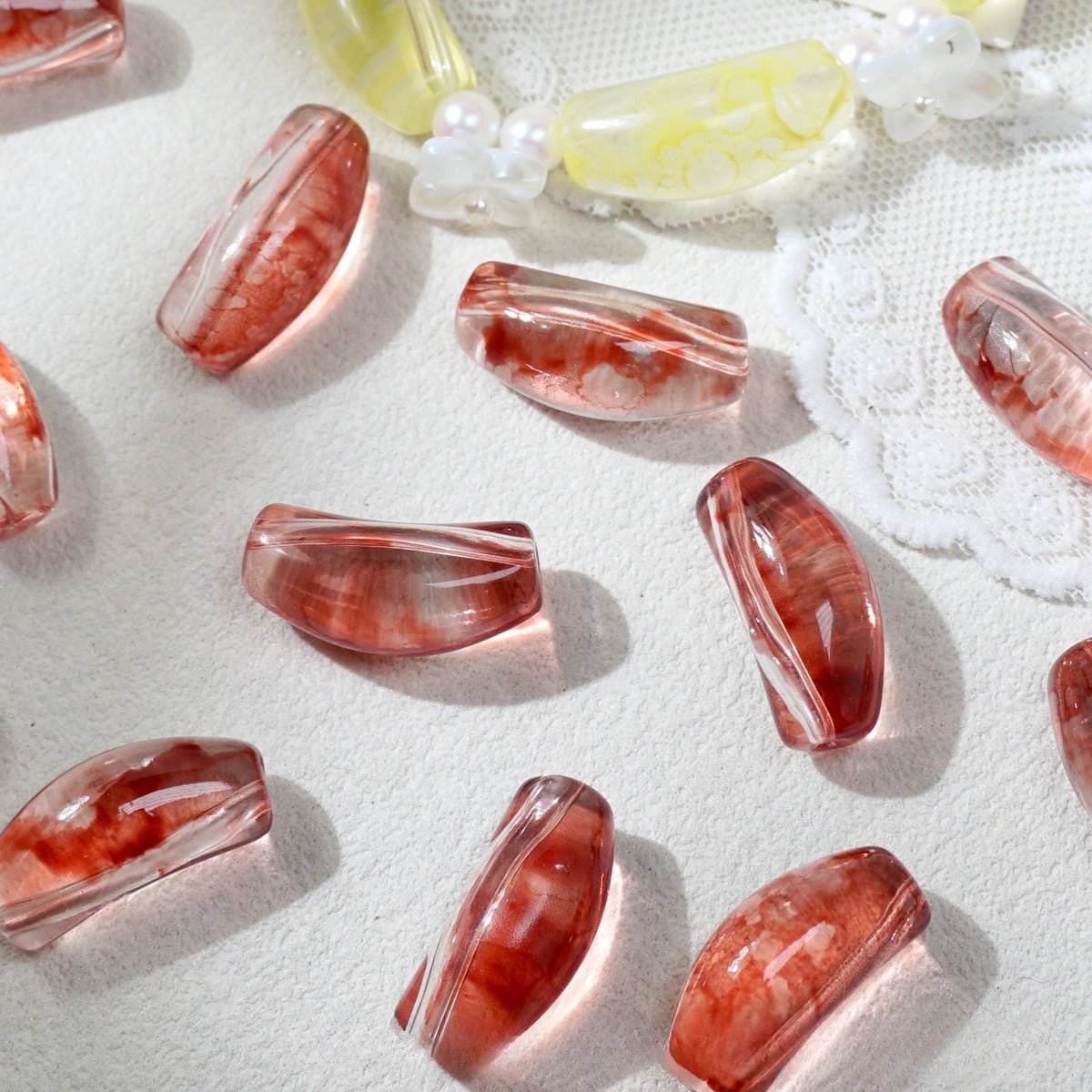 Translucent red marbled curved glass tube beads scattered on white textured fabric