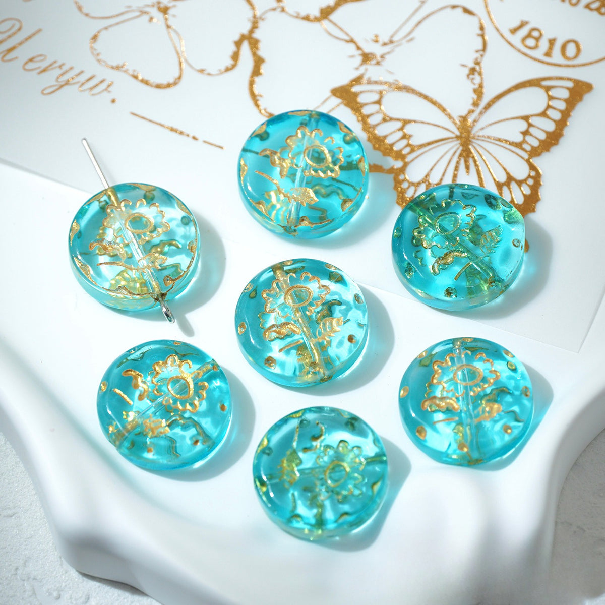 Seven lake blue 18mm gold-painted Czech-style glass sunflower beads on a white decorative surface