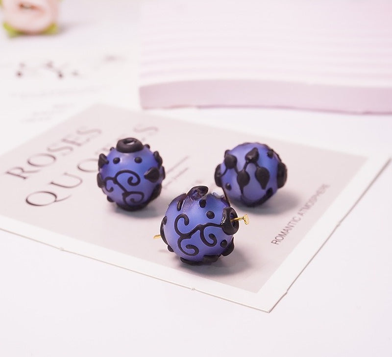 Three purple and black patterned spherical beads displayed on a decorative card on a white surface.
