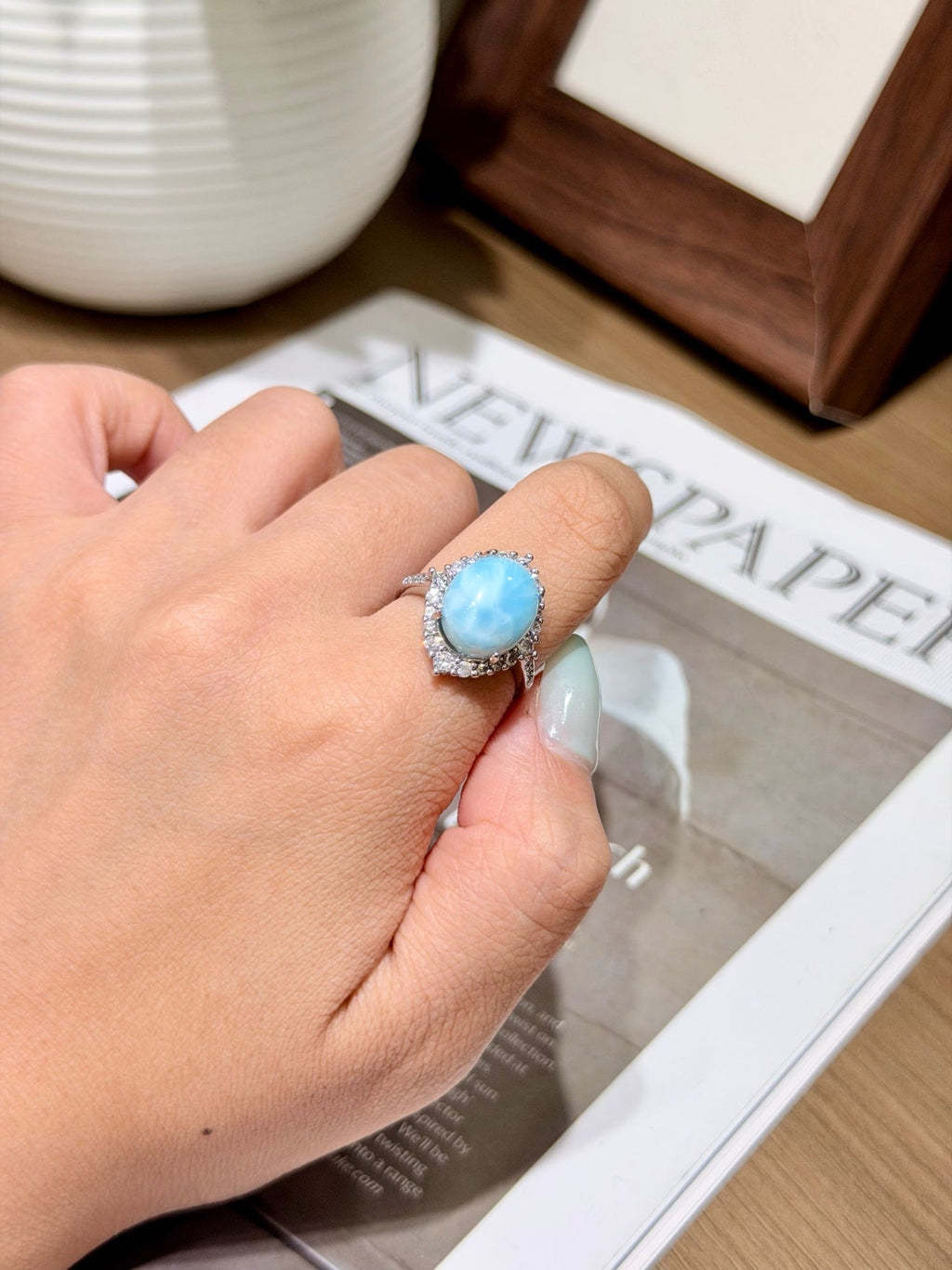 Oval light blue marbled larimar ring with a clear stone halo, worn on a hand