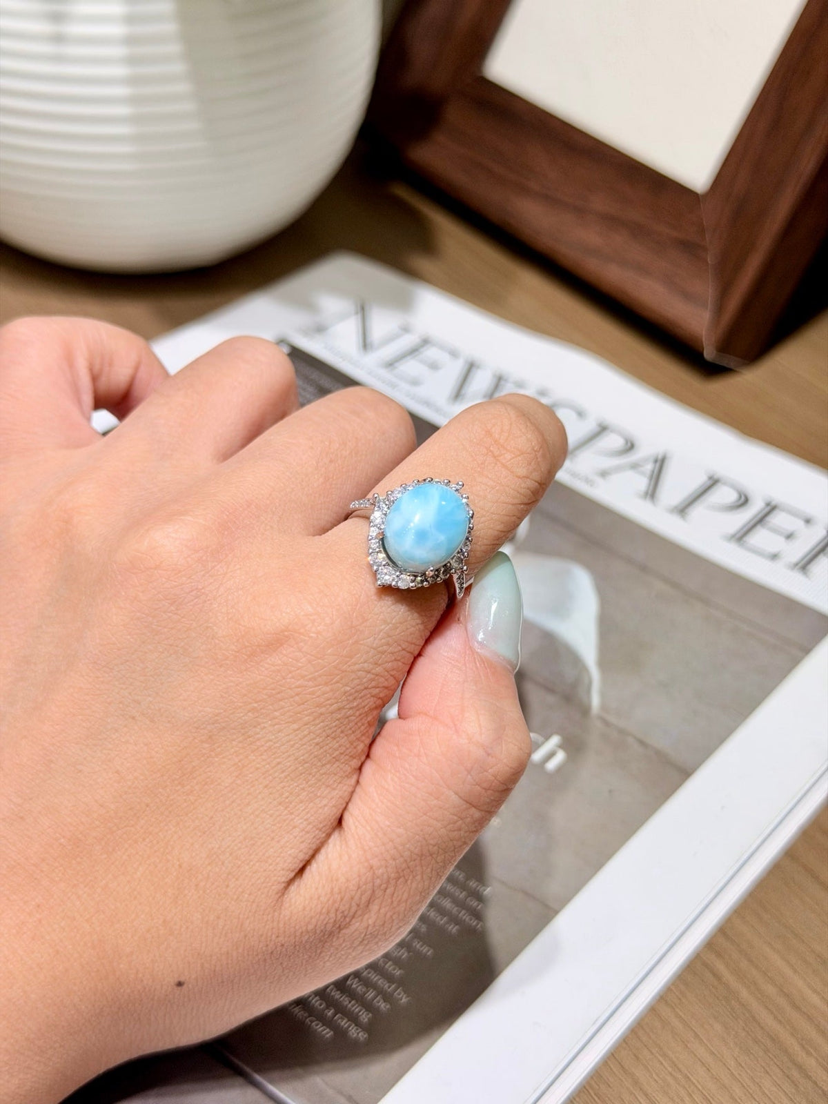Oval light blue marbled larimar ring with a clear stone halo, worn on a hand