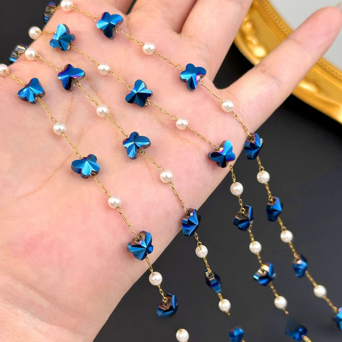 Gold chain strands with metallic blue butterfly charms and white pearls draped over an open hand