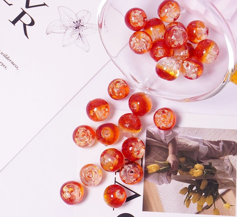 Red-orange two-tone glow-in-the-dark glass beads spilling from a glass cup onto a floral printed card