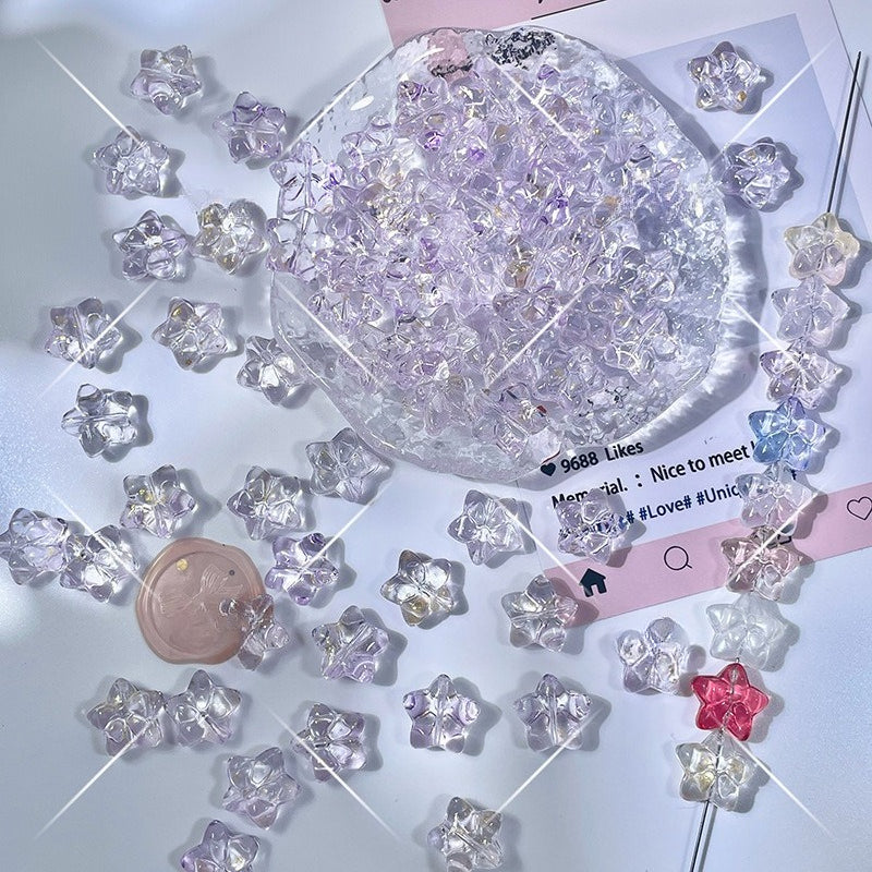 Clear star-shaped glass beads with lavender tint and pink and red accents on a white surface