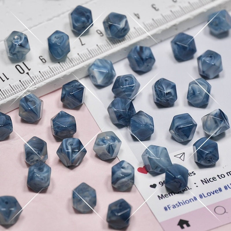 Small faceted blue marbled beads scattered on a pink and white surface with a ruler