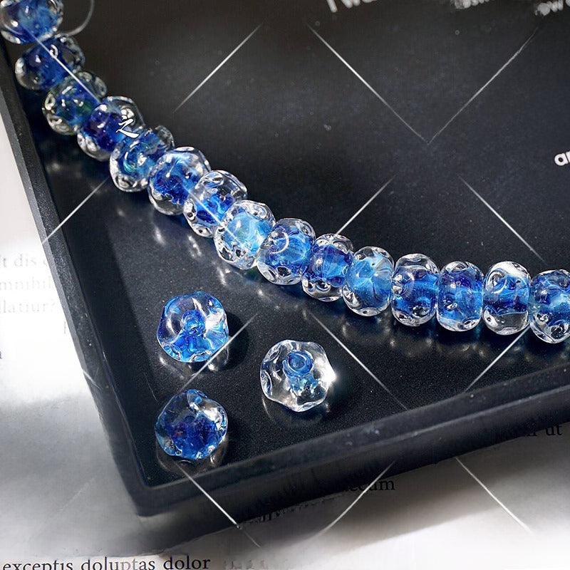 Strand of blue and clear water-ripple lampwork glass beads on a black tray with three loose beads in front