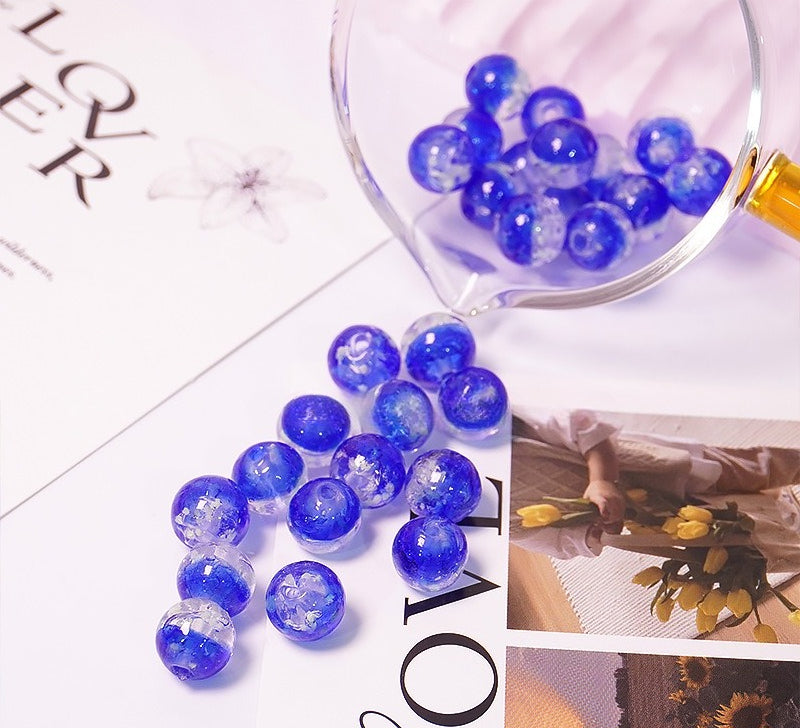 Blue two-tone glow-in-the-dark glass beads spilling from a glass cup onto a printed card