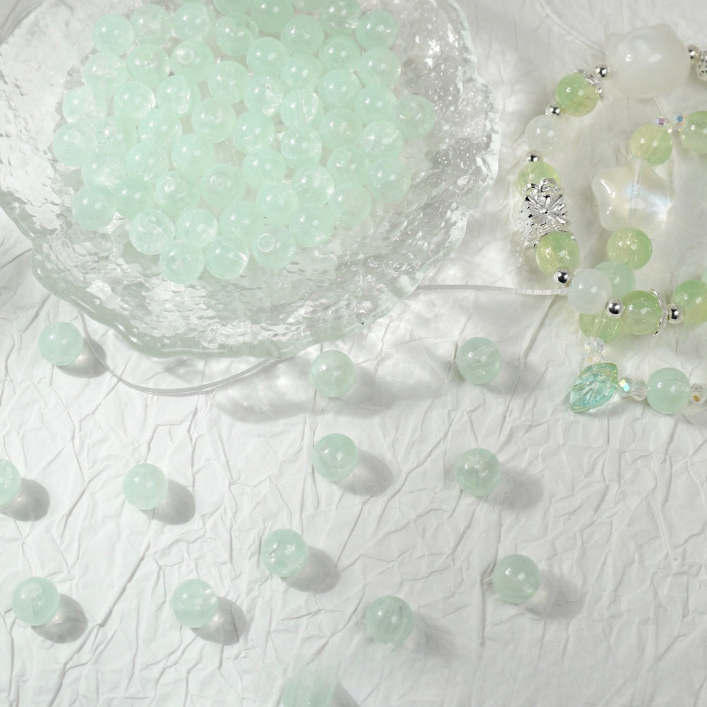 Light green translucent round glass beads in a bowl with a beaded bracelet