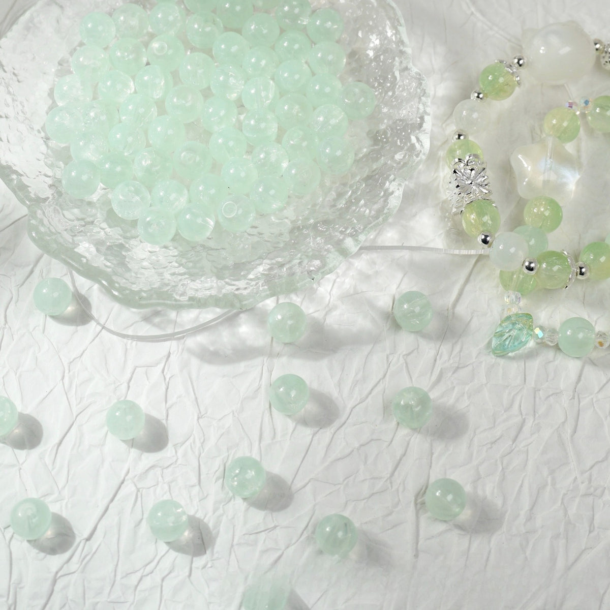 Light green translucent round glass beads in a bowl with a beaded bracelet