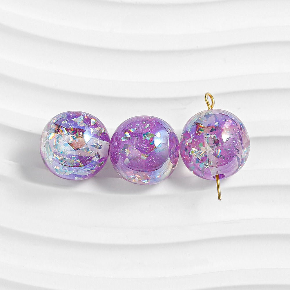 Three purple glitter resin beads on white; right bead has gold loop at top