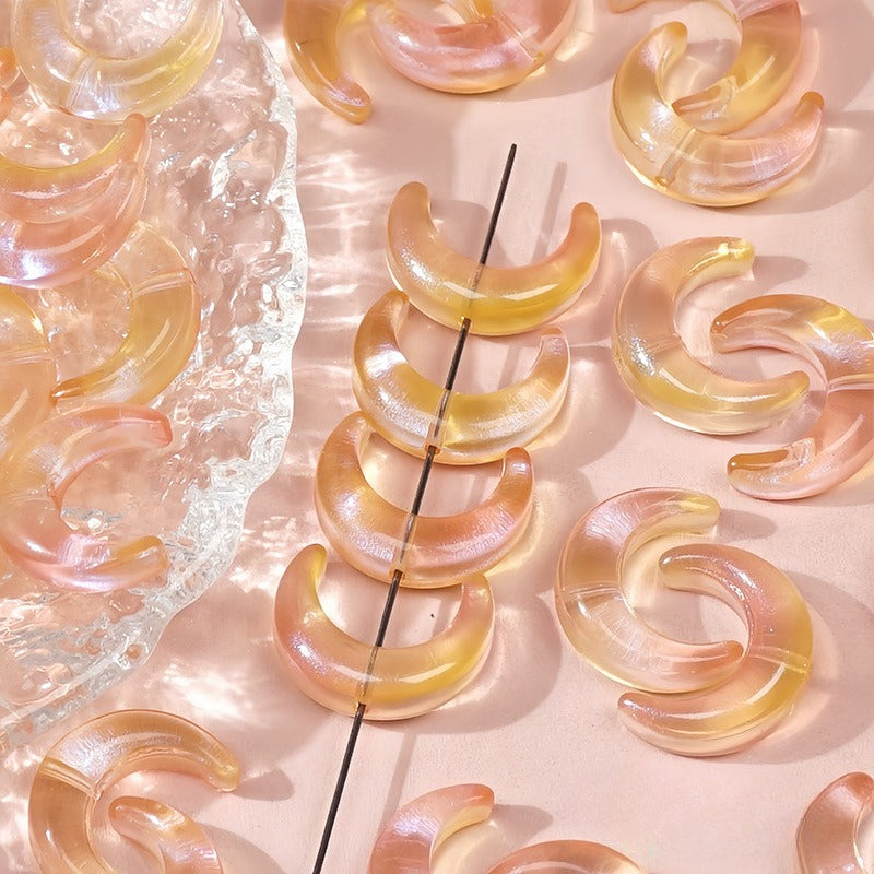 Peach and yellow translucent glazed glass crescent moon beads, some strung on a wire and others on a pink surface
