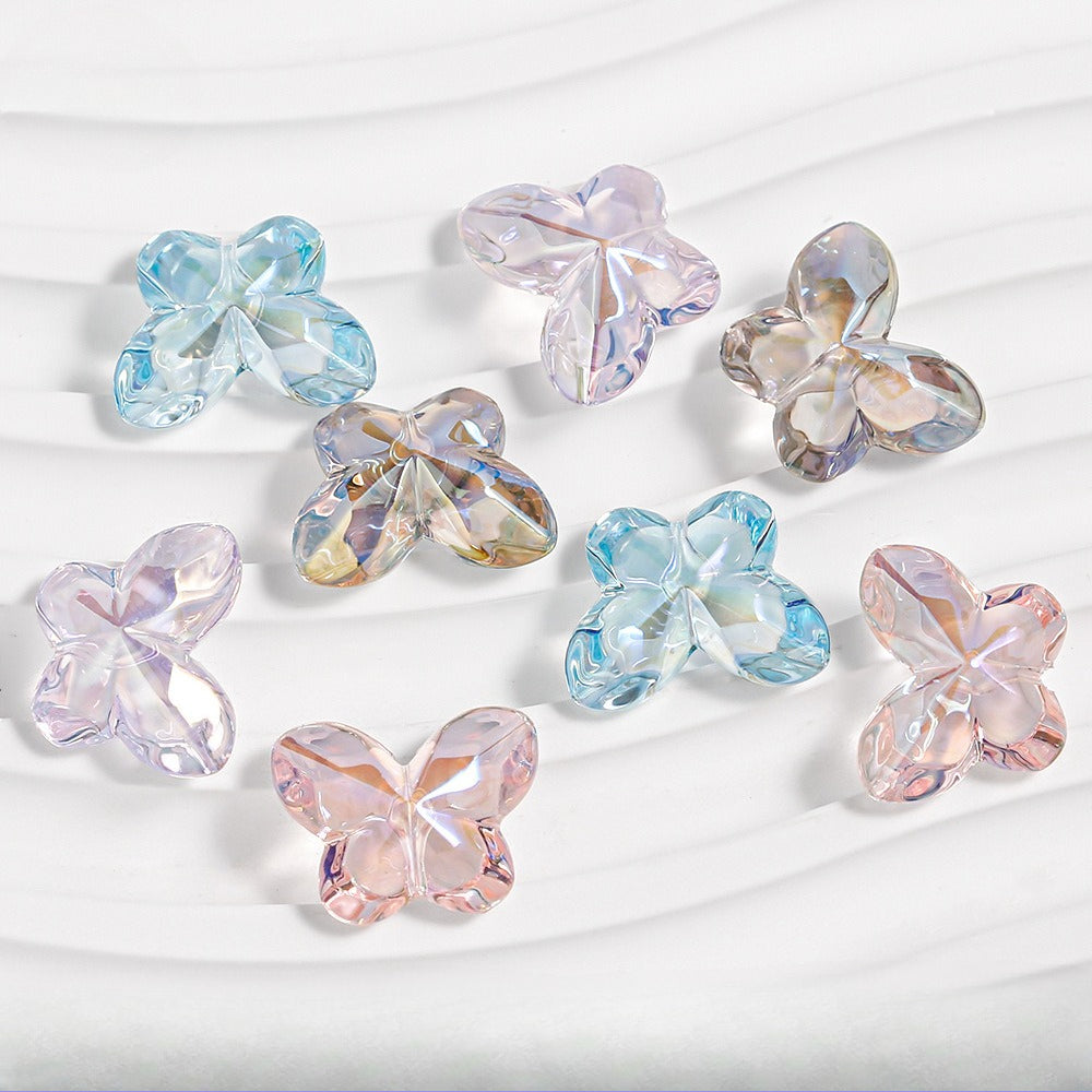 Nine faceted butterfly-shaped beads in pastel blue, pink, lavender and iridescent tones on white textured fabric