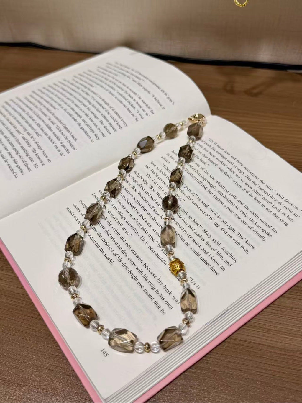 Smoky quartz beaded necklace with faceted brown and clear quartz beads and gold spacers on an open book