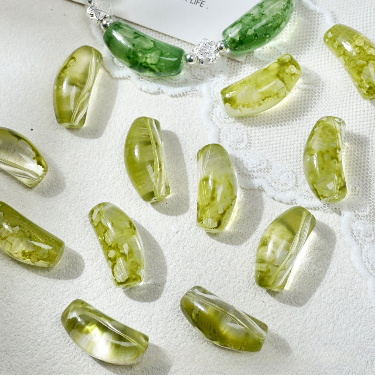 Translucent olive green curved glass tube beads with inclusions on white textured fabric