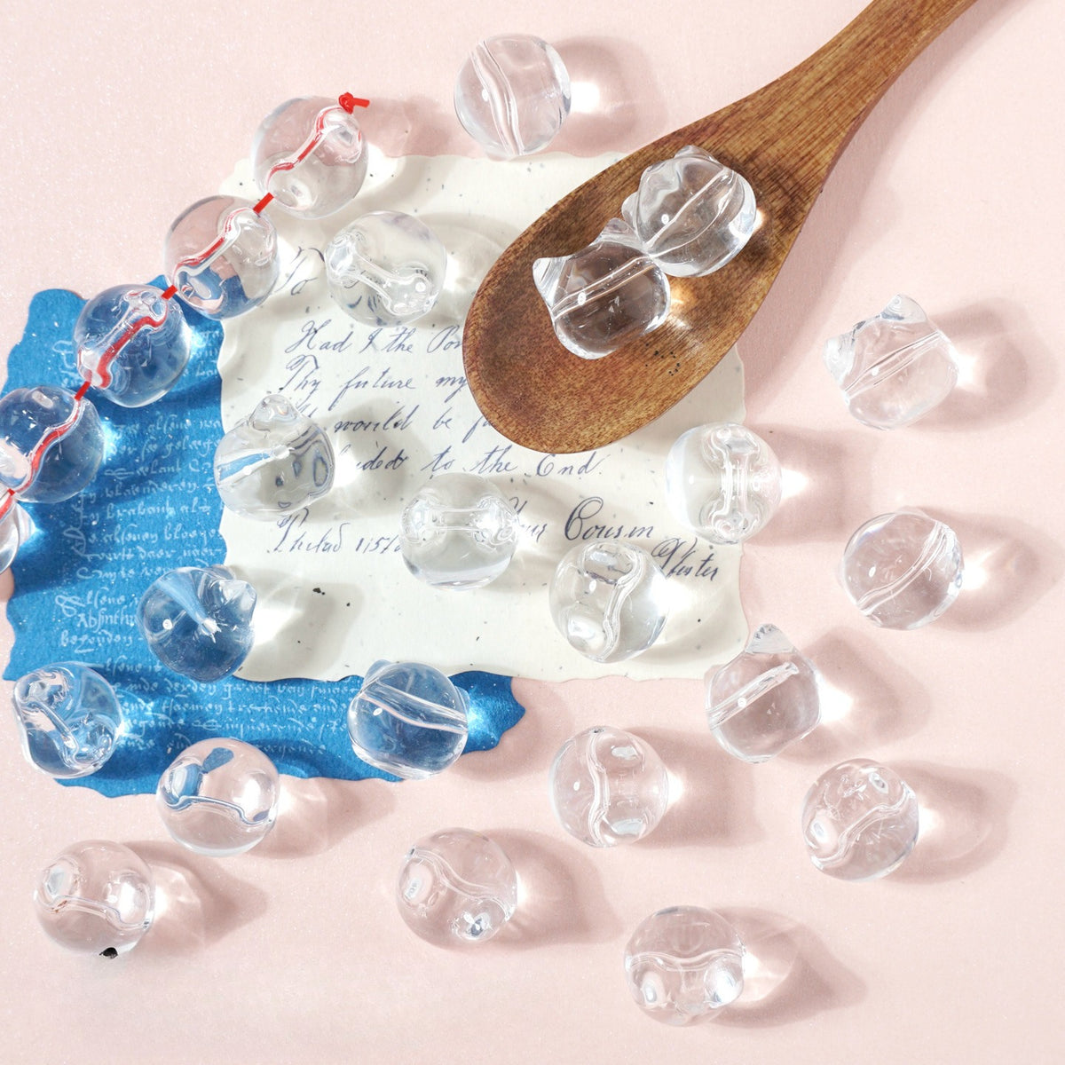 Clear glass marbles on light pink with a wooden spoon, vintage note and blue cloth