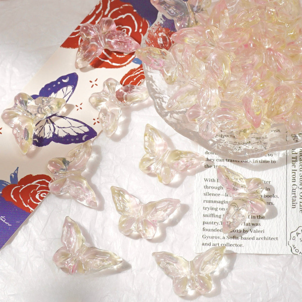 Clear iridescent butterfly-shaped beads scattered on a white textured surface next to a glass bowl