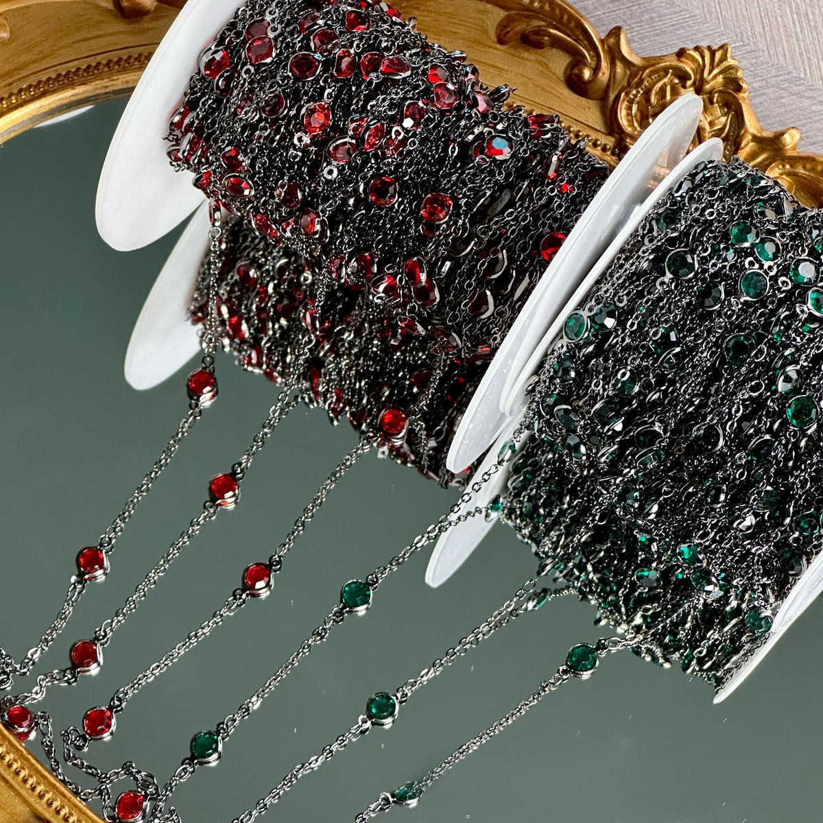 Two spools of silver chain trim embellished with red and green rhinestones, draped over a decorative gold mirror.
