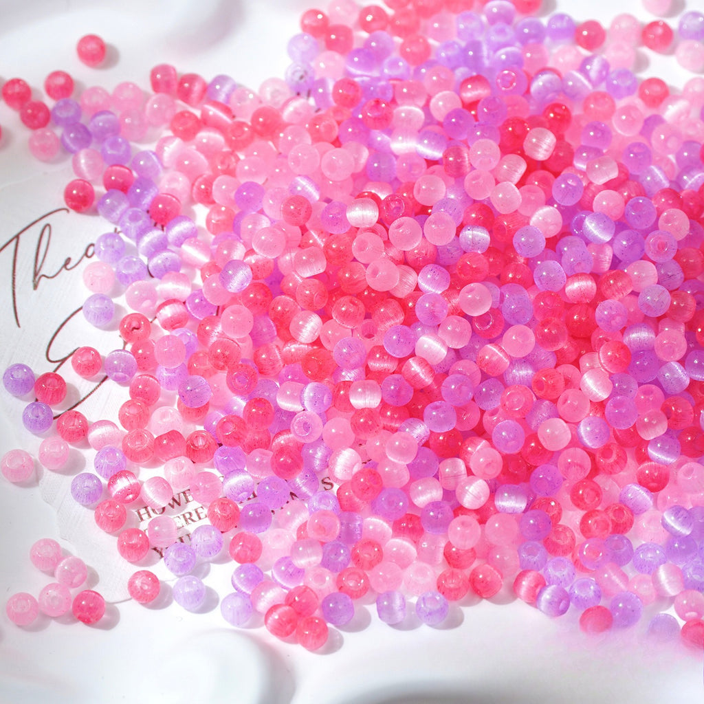 Close-up pile of frosted pink and lavender-purple cat's-eye glass beads on white surface
