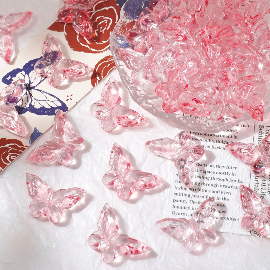 Pink butterfly-shaped glass beads scattered on white surface with glass bowl