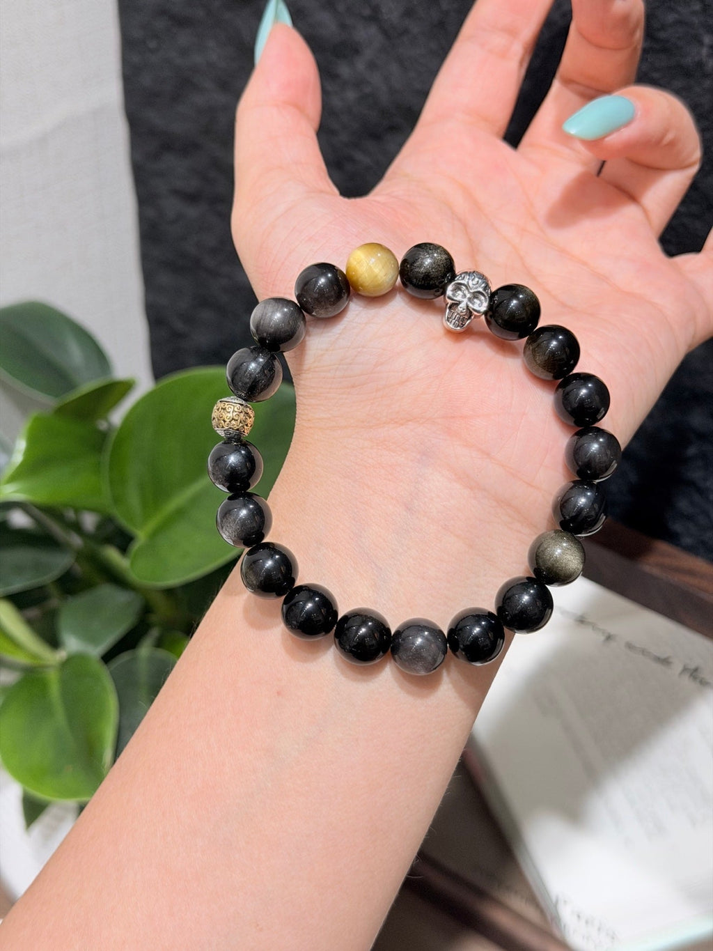 Hand holding black beaded bracelet with gold accent bead and silver skull charm