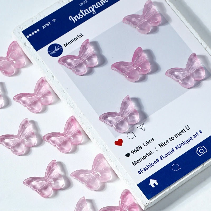 Pink translucent butterfly-shaped glass beads on a white surface next to a printed card