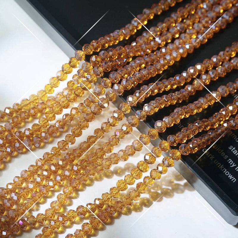 Multiple strands of faceted amber crystal glass wheel beads arranged diagonally on white surface