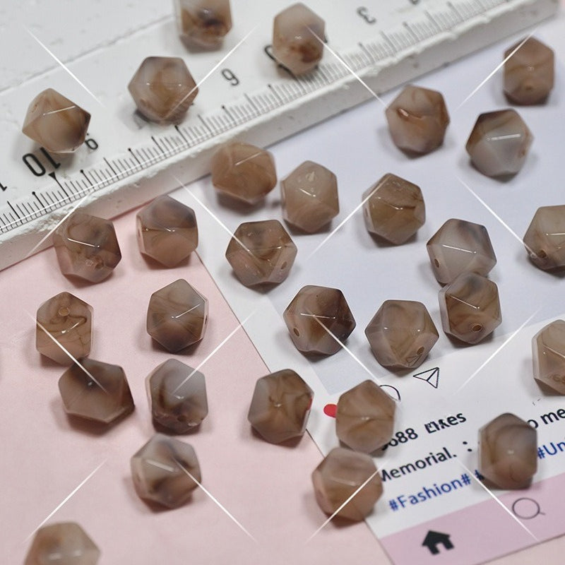 Faceted hexagonal beads in smoky brown and gray scattered on a white and pink surface with a ruler