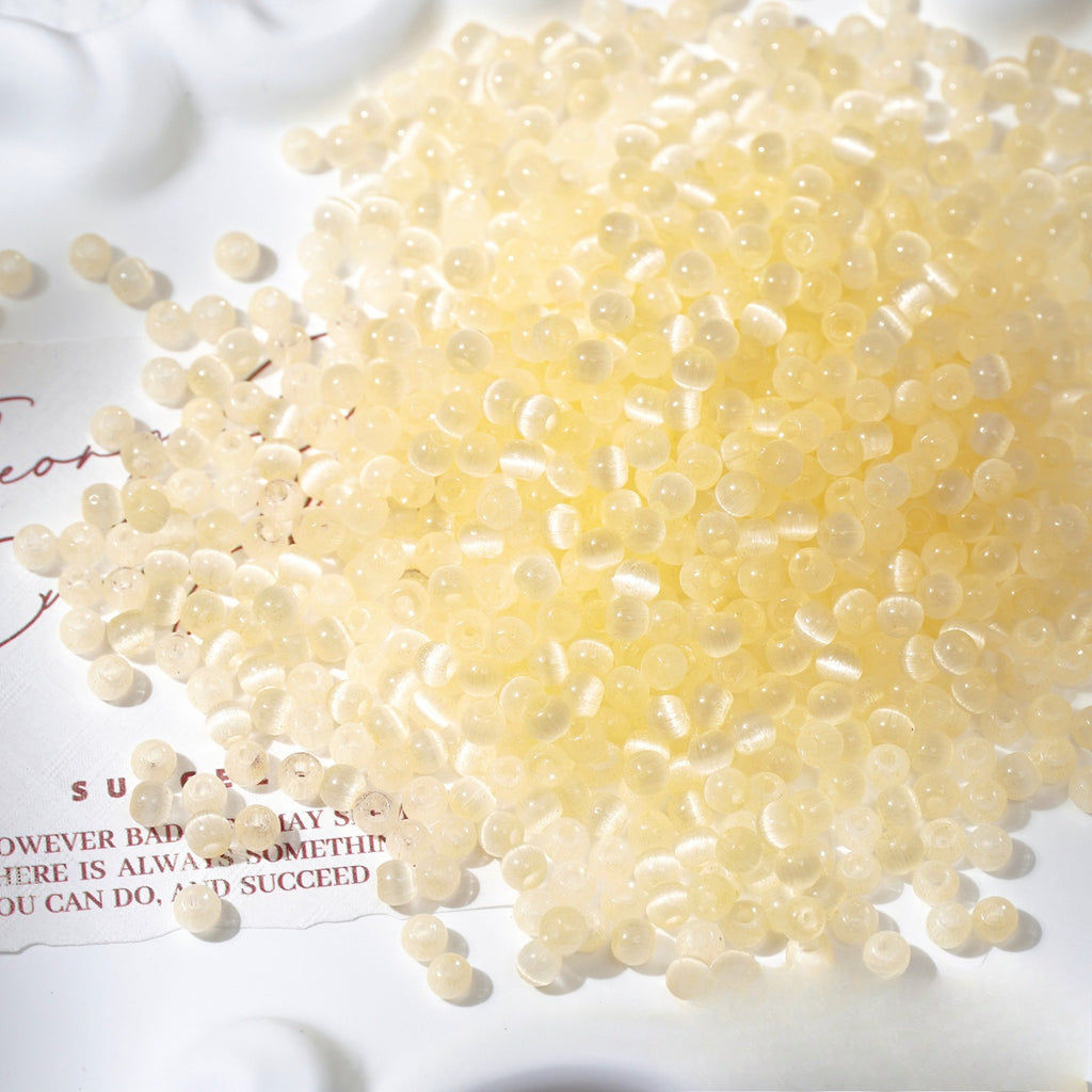 Close-up pile of frosted lemon-yellow cat's-eye glass beads on white surface
